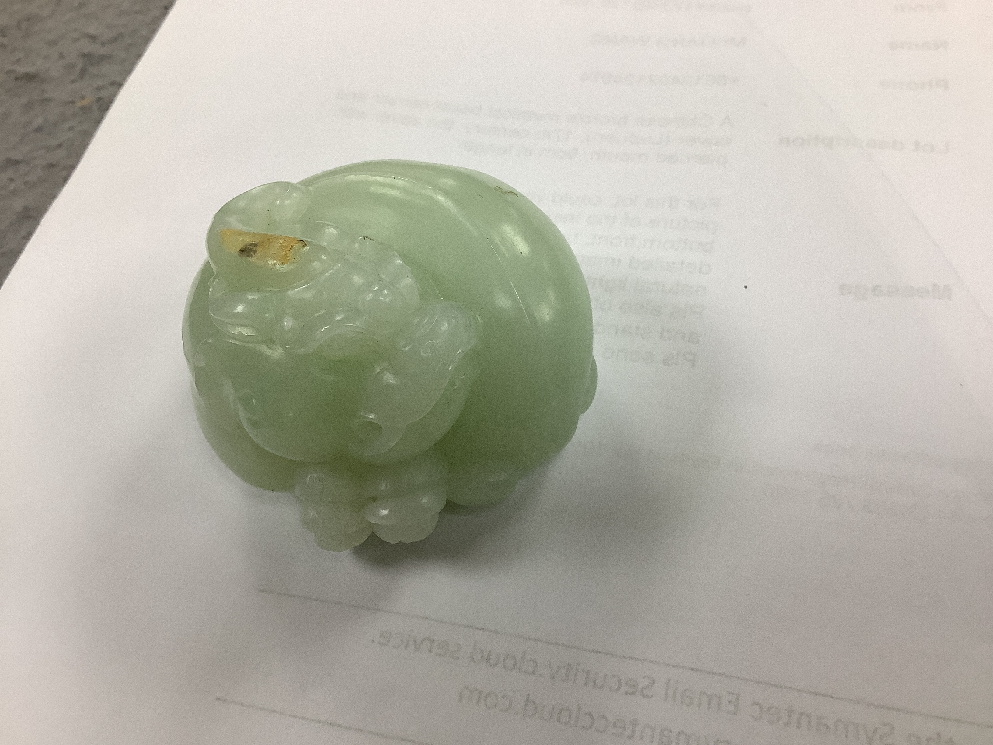 A Chinese celadon jade carving of a lion-dog, in recumbent pose, its crest with a russet inclusion, 5.3cm